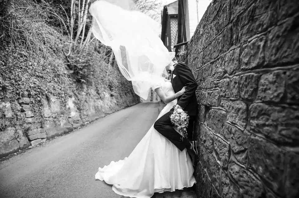 Lucy & Michael 9 Bride and groom sneak a kiss in a back alley leaning on old stone wall - Scott Gilbert Wedding Photography
