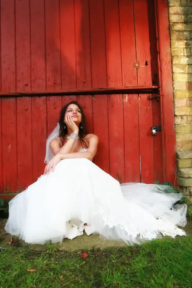 Bride reflects on the day whilst sat in front of large red barn door - Scott Gilbert Wedding Photography