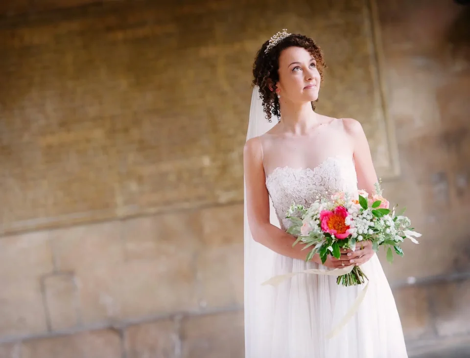 Bride holds elegant flowers in front of stone wall - Scott Gilbert Wedding Photography