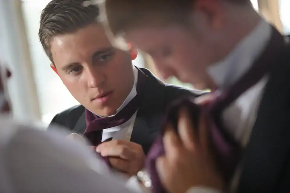 Two men in formal suits adjusting ties, showcasing men's fashion.