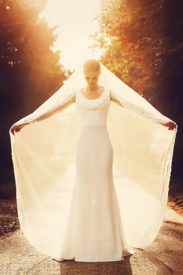 Bride holds open her veil as sunlight beams through from behind - Scott Gilbert Wedding Photography