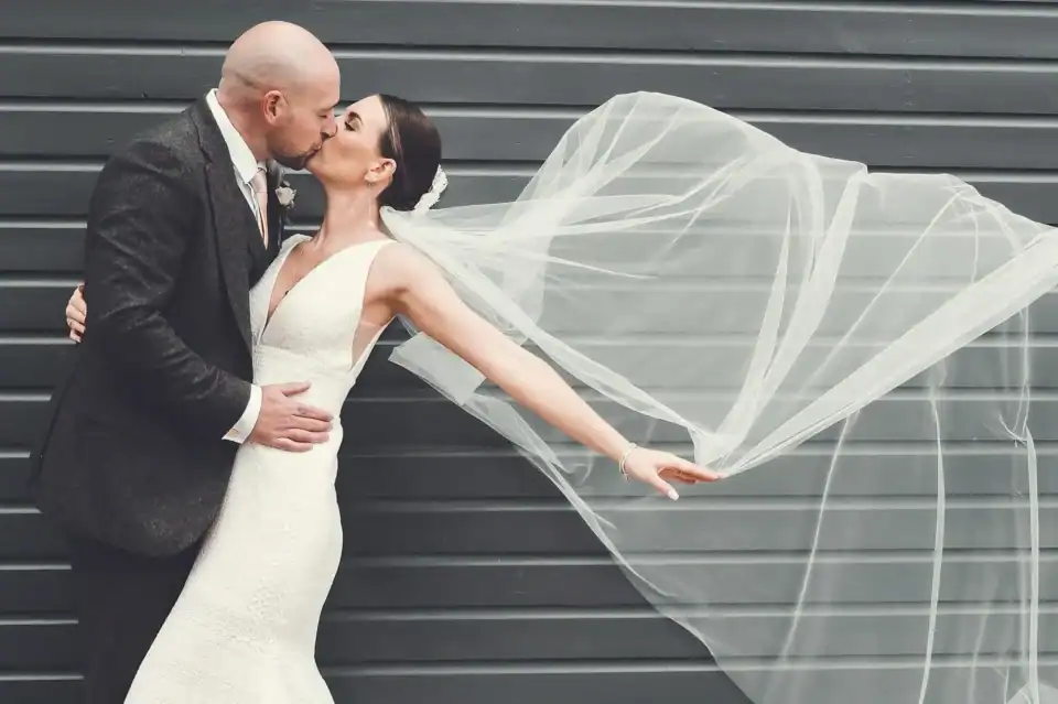 Bride and groom kiss in front of barn with veil floating in wind - Scott Gilbert Wedding Photography