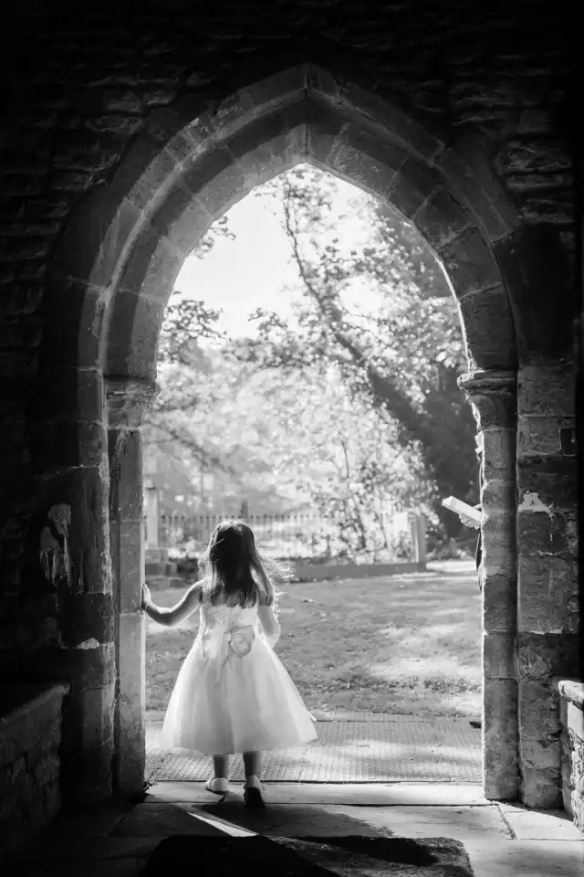 Flower girl standing at the entrance to the countryside church - Scott Gilbert Wedding Photography