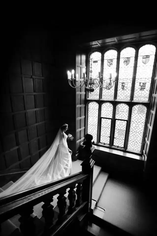 Bride walking down staircase in front of huge stain glass windows of venue in main hall - Scott Gilbert Wedding Photography