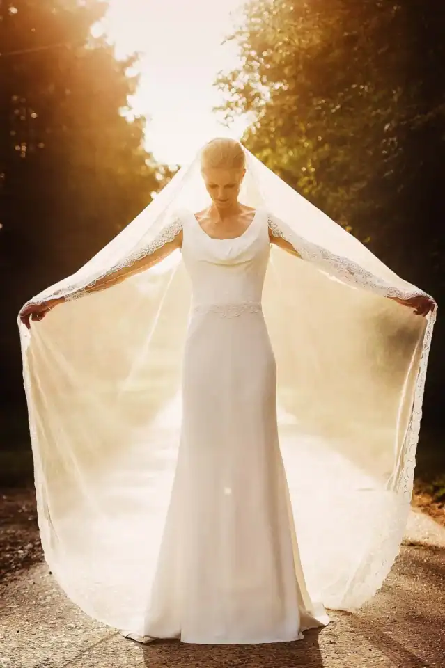 Bride holds her veil open wide as the wunlight beams on it from behind - Scott Gilbert Wedding Photography