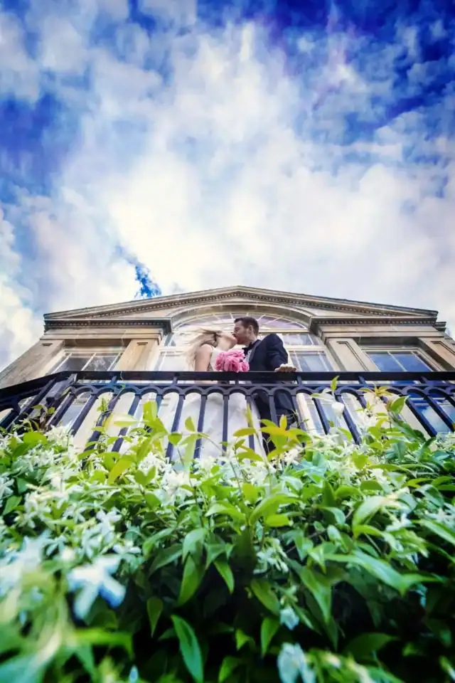 Newly weds kissing on balcony with beautiful cloudy skies above - Scott Gilbert Wedding Photography