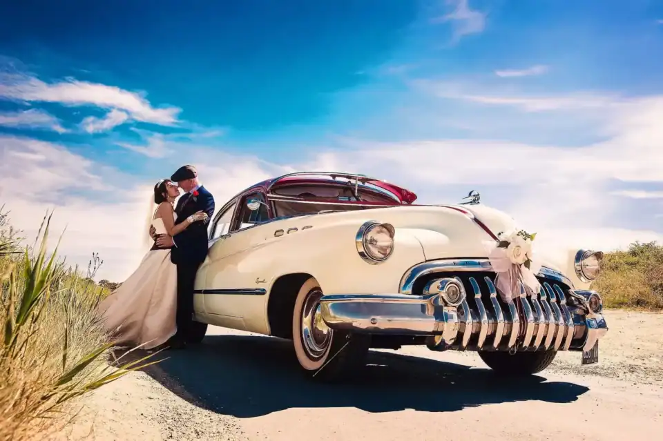 Newly weds kissing whilst leaning on old classic cream car - Scott Gilbert Wedding Photography