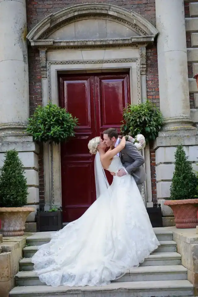 Bride and groom kiss on the steps to their venue in front of red wooden door - Scott Gilbert Wedding Photography